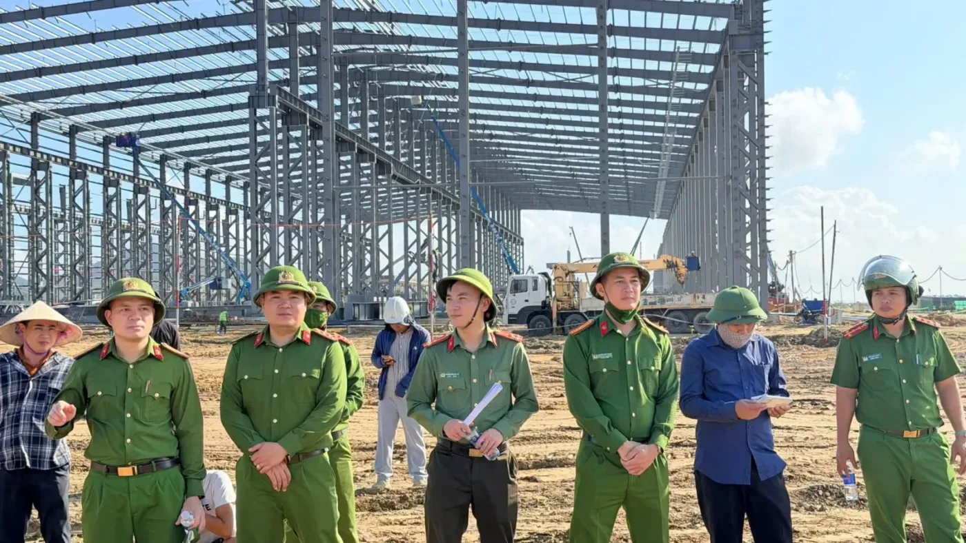 Lực lượng chức năng phường Vũng Áng đứng trên khu đất san lấp, phía sau là khung nhà xưởng thép đang dựng