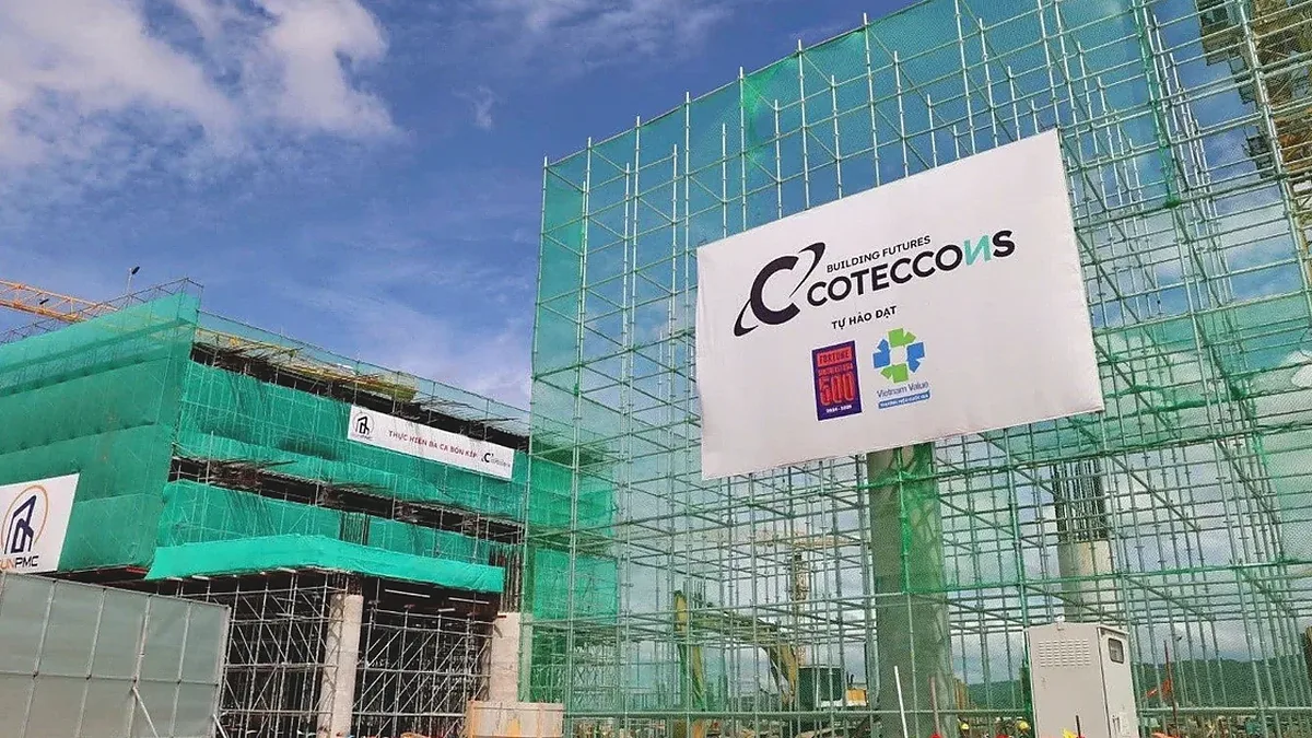 Công trường Coteccons với giàn giáo phủ lưới xanh và biển hiệu Coteccons trước tòa nhà đang xây